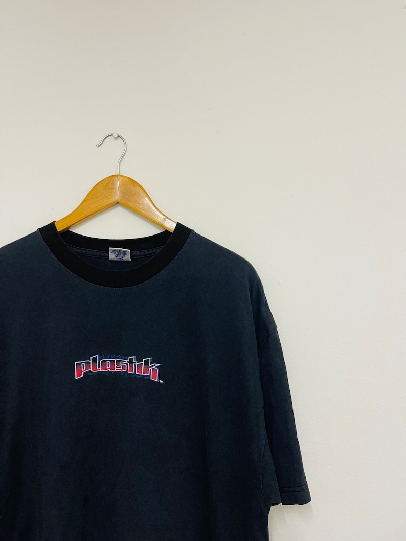 May include: Black t-shirt with a red and blue "plastik" logo printed on the front.