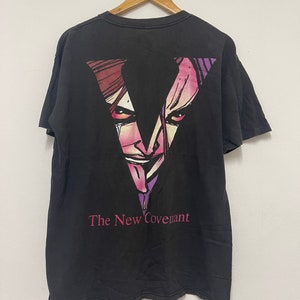 Puede incluir: Camiseta negra con un estampado gráfico de una cara estilizada en tonos morados y rosas. El texto "The New Covenant" está impreso debajo del gráfico.