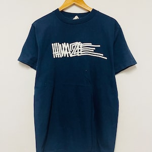 Puede incluir: Una camiseta azul marino con un gráfico blanco de la palabra "HIMAZE" escrita en una fuente estilizada.