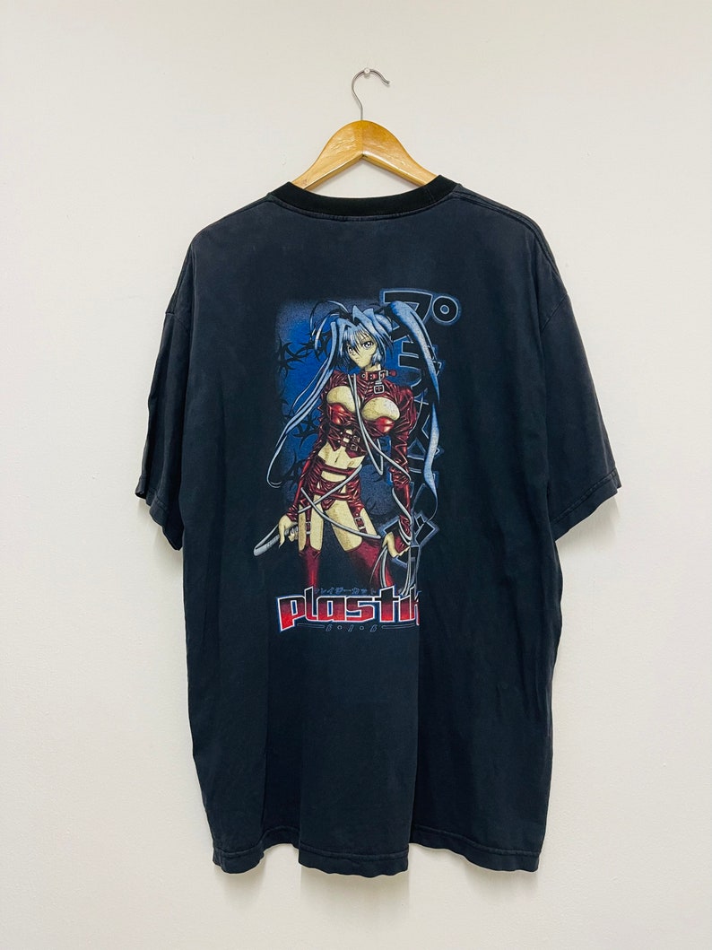 May include: Black t-shirt with a graphic print of an anime character with blue hair and a red outfit. The text "Plastic" is printed below the character.