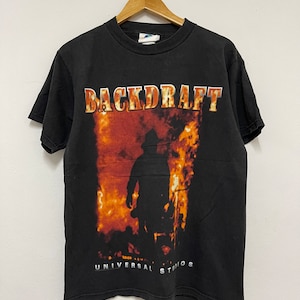 May include: Black t-shirt with a graphic of a firefighter walking through flames. The text "BACKDRAFT" is printed in yellow above the graphic and "UNIVERSAL STUDIOS" is printed in white below the graphic.
