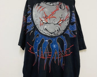 May include: Black t-shirt with a graphic print of a grey moon with a red and blue design. The moon has a face with a nose ring and red eyes.