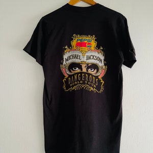 May include: Black t-shirt featuring a colorful graphic promoting the Michael Jackson Dangerous World Tour, presented by Pepsi. The design includes the Pepsi logo, Michael Jackson's name, and the tour title in gold lettering.