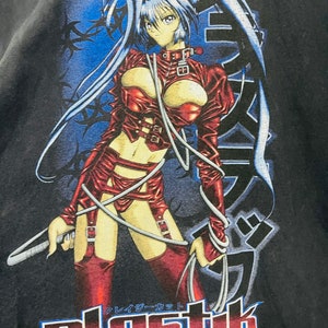 May include: A black t-shirt with a graphic print of an anime character in a red leather outfit. The character is holding a whip and has long blue hair. The text "plastik" is printed in red and blue below the character.