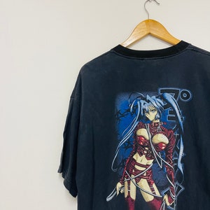 May include: Black t-shirt with a graphic print of an anime character in a red leather outfit. The character is holding a whip and the text "Plastic" is printed below her.