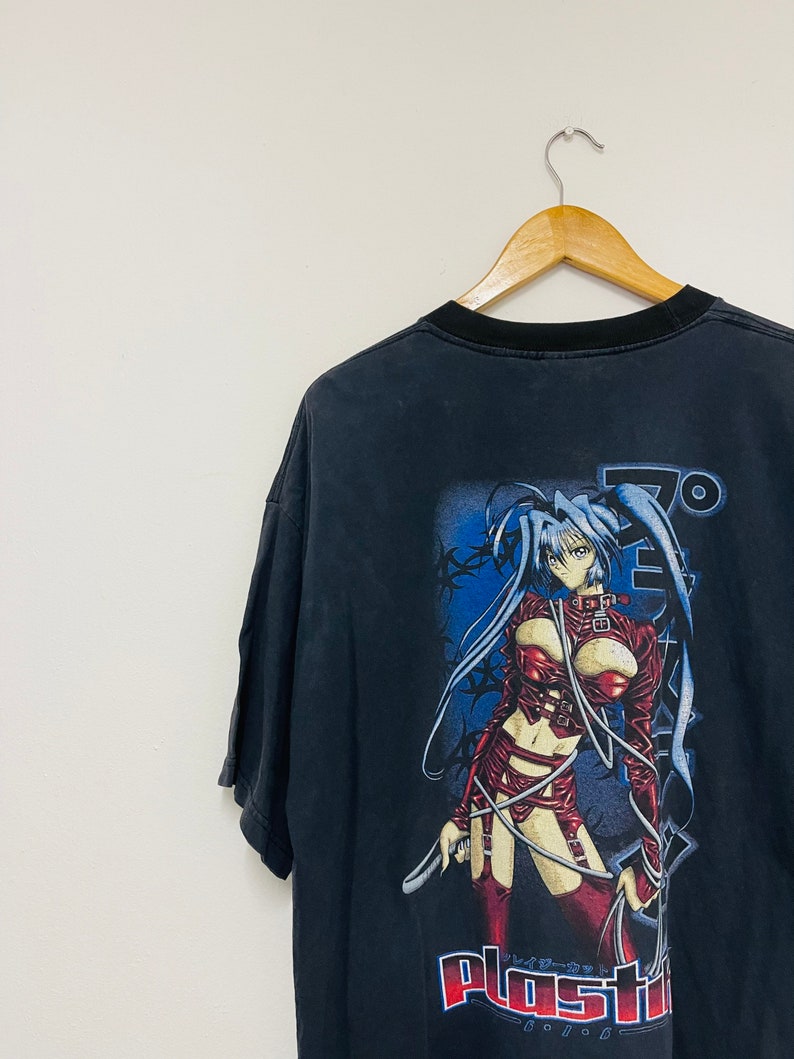 May include: Black t-shirt with a graphic print of an anime character in a red leather outfit. The character is holding a whip and the text "Plastic" is printed below her.