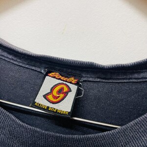 May include: Close-up of a black t-shirt collar with a tag. The tag features the brand name "Souls" in red and yellow, with a stylized "G" logo. The text "ACTIVE and WORK" is also visible on the tag.