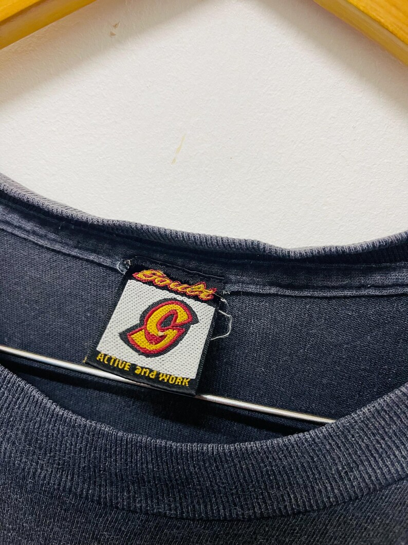 May include: Close-up of a black t-shirt collar with a tag. The tag features the brand name "Souls" in red and yellow, with a stylized "G" logo. The text "ACTIVE and WORK" is also visible on the tag.
