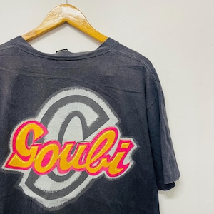 May include: Dark gray t-shirt with a large graphic on the back. The graphic features the word "Goubi" in a vibrant pink and yellow font, outlined in orange, set against a gray and white circular design.