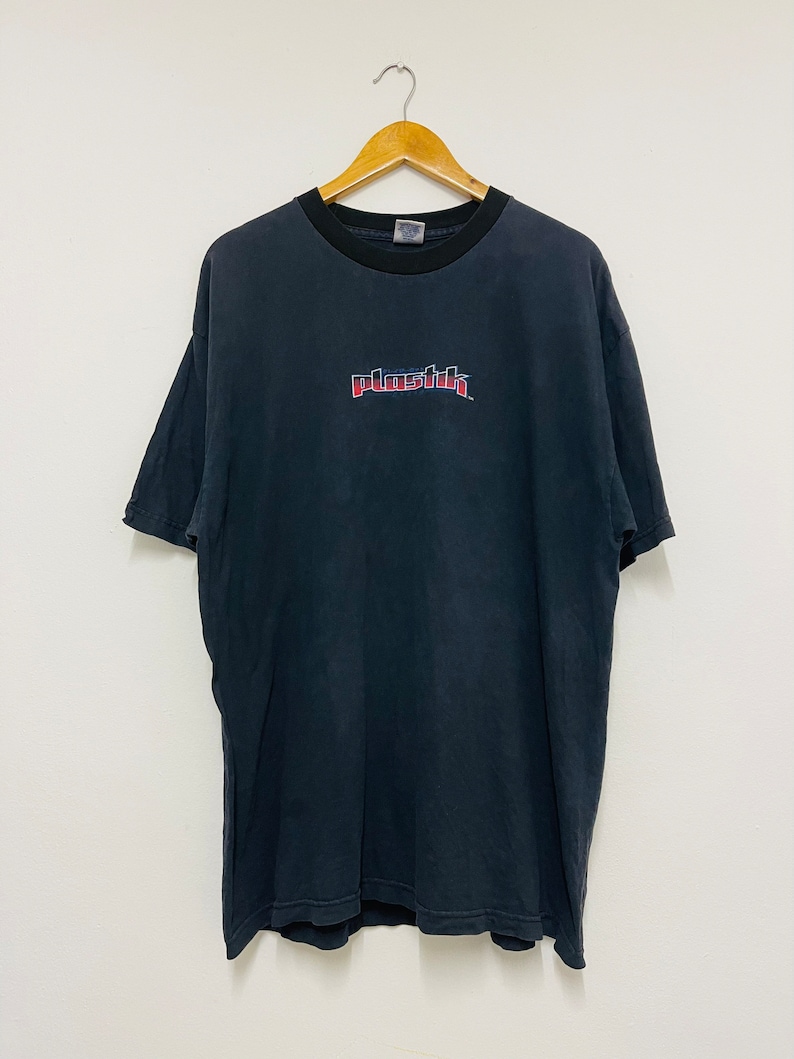 May include: Black t-shirt with a red and blue "Plastik" logo printed on the front.