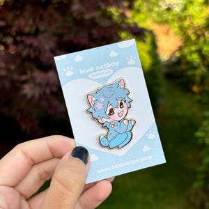 Op de afbeelding: Blauwe catboy emaille pin met een blauwe kat die een roze strik en een blauwe en witte outfit draagt. De pin is op een witte kaart met de tekst "blue catboy enamel pin" en "www.beebeezed.shop".