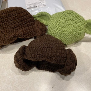 May include: Three crocheted hats, one brown, one green, and one brown with two brown loops on the sides.