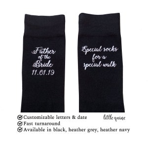 Può includere: Un paio di calzini neri con testo bianco. Un calzino dice "Father of the Bride 11.01.19" e l'altro calzino dice "Special socks for a special walk". I calzini sono personalizzabili con lettere e una data. Sono disponibili in nero, grigio melange e blu melange.