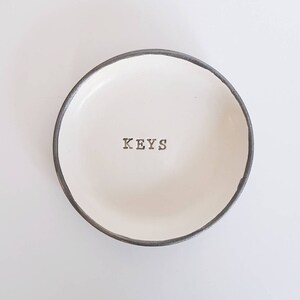 May include: White ceramic dish with a black rim and the word "KEYS" inscribed in the centre.