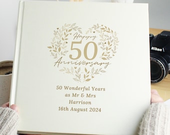 May include: A cream-coloured photo album with a gold heart design and the text "Happy 50th Anniversary". The album also includes the text "50 Wonderful Years as Mr & Mrs Harrison 16th August 2024".