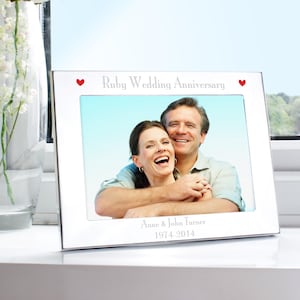May include: A silver picture frame with the text "Ruby Wedding Anniversary" and two red heart symbols. The frame holds a photo of a smiling couple. The names "Anne & John Turner" and the years "1974-2014" are engraved on the frame.