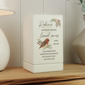 May include: A white ceramic memorial box with the text "Robins Appear When Loved Ones Are Near." It features a watercolor illustration of a robin and foliage. The box also includes the name "JULIE ANNE SHAW" and dates.