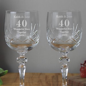 May include: Two crystal wine glasses with engraved text. Each glass features the inscription "Keith & Jane", "40", "Wonderful Years Together 2024". The glasses have a diamond-cut pattern and faceted stems. The background is a neutral tone.