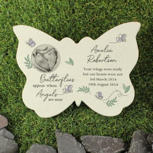 May include: A white butterfly-shaped memorial stone with a photo of a baby's feet. The stone has the text "Butterflies appear when Angels are near" and "Amelia Robertson Your wings were ready but our hearts were not 3rd March 2024 18th August 2024".