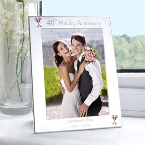 May include: Silver picture frame displaying a photograph of a smiling couple. The frame is inscribed with "40th Wedding Anniversary", the couple's names, and the years 1974-2014. Two red cocktail glasses are at the top and bottom.