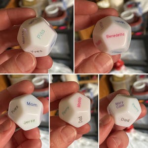 Puede incluir: Un dado blanco de m&uacute;ltiples caras con varios nombres impresos en diferentes colores en cada cara, incluyendo nombres como Pita, Marta, Yves, Mom, Benedetta, Lottie, Maddy, Jerzy, Penny, Dad y Mary Cate, con un acabado liso y opaco.
