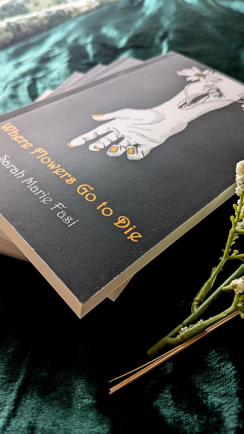 Może przedstawiać: Książka zatytułowana "Where Flowers Go to Die" autorstwa Sarah Marie Fasi. Okładka jest czarna z białą ilustracją dłoni i złotymi akcentami. Książka jest ułożona na innych książkach, z gałązką białych kwiat&oacute;w na pierwszym planie.