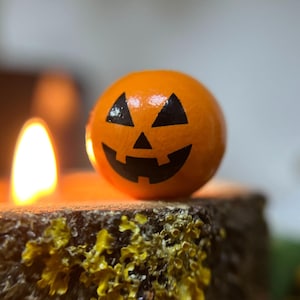 May include: A small orange pumpkin with a carved jack-o'-lantern face sits on top of a wooden stump with a lit candle in front of it.