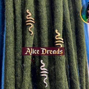 Può includere: Due perline per dreadlock a forma di serpente, dorate e argentate, su uno sfondo di dreadlock verdi e blu. Le perline sono progettate per essere utilizzate come gioielli per capelli.