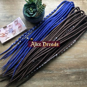 May include: A set of brown and blue synthetic dreadlocks with white stitching. The dreadlocks are arranged in a fan shape and have beads at the ends.