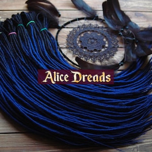 May include: A set of blue and black synthetic dreadlocks, with the blue colour fading to black. The dreadlocks are arranged in a fan shape and are lying on a wooden surface. The text "Alice Dreads" is visible in the image.
