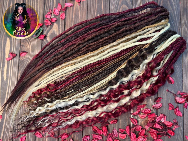 May include: A set of synthetic dreadlocks in various shades of brown, red, and blonde. The dreadlocks are arranged in a fan shape on a wooden surface with red flower petals scattered around.