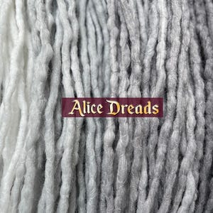 May include: A close-up of two sets of synthetic dreadlocks, one white and one gray, with the text "Alice Dreads" in a gold banner.