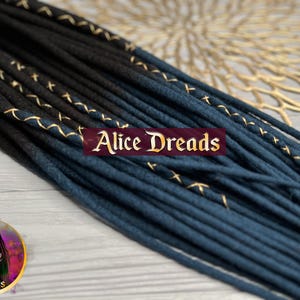 May include: Black and dark blue synthetic dreadlocks with gold thread accents. The dreadlocks are arranged in a fan shape and are lying on a wooden surface.