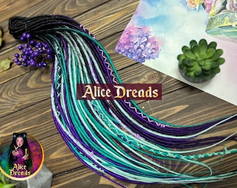 May include: A set of synthetic dreadlocks in black, teal, purple, and white. The dreadlocks are arranged in a fan shape on a wooden surface. The text "Alice Dreads" is visible in the image.