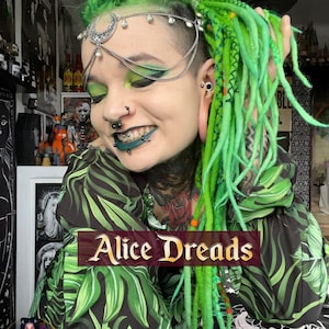 May include: A person with green dreadlocks and a silver headpiece with a crescent moon design. They are wearing a green and black floral print shirt. The text "Alice Dreads" is visible in the image.