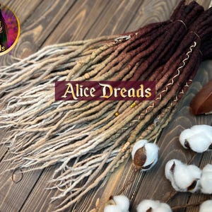 May include: A set of brown and beige synthetic dreadlocks with gold accents. The dreadlocks are arranged in a fan shape on a wooden surface.