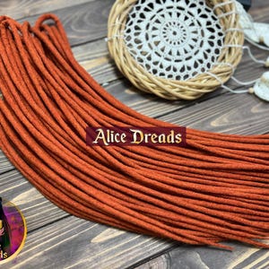 May include: A bundle of 24 terracotta-colored synthetic dreadlocks. The dreadlocks are made of a soft, textured material and are approximately 24 inches long.