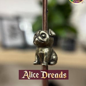May include: A small, gold-coloured pug charm, sitting on a copper-coloured rod. The charm is detailed with a cute, cartoon-like face and has a textured finish.