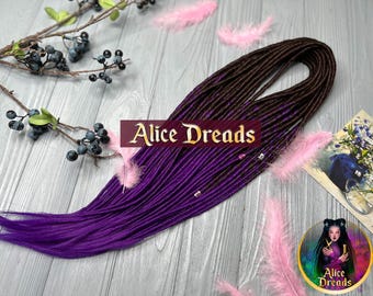 May include: Purple and brown synthetic dreadlocks with beads. The dreadlocks are arranged in a long, flowing style. The background is a wooden surface with pink feathers.
