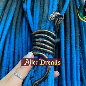 May include: Blue and black dreadlocks with a silver snake hair accessory. The accessory is wrapped around the dreadlocks. The text "Alice Dreads" is visible in the image.