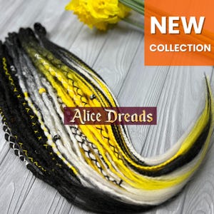 May include: Black, white and yellow synthetic dreadlocks with black stitching. The dreadlocks are arranged in a fan shape and have beads at the ends. The text "Alice Dreads" is visible in the image.