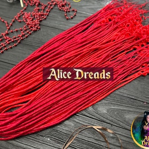 Pode incluir: Um pacote de dreadlocks sintéticas de cor vermelha brilhante, com alguns cachos nas pontas. As dreadlocks estão dispostas em forma de leque sobre uma superfície de madeira escura. O texto "Alice Dreads" é visível no centro da imagem.