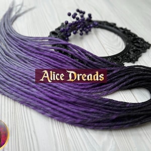 May include: A set of ombre synthetic dreadlocks with a gradient from light purple to dark purple and black. The dreadlocks are arranged in a fan shape on a white wooden surface. The text "Alice Dreads" is visible in the image.