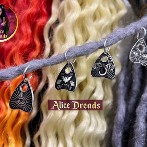 Può includere: Tre ciondoli in metallo color argento a forma di planchette fissati a un dread sintetico grigio. I ciondoli presentano dettagli in smalto nero tra cui un occhio, un pipistrello e un muso di gatto, con il testo GOODBYE visibile su due pezzi.