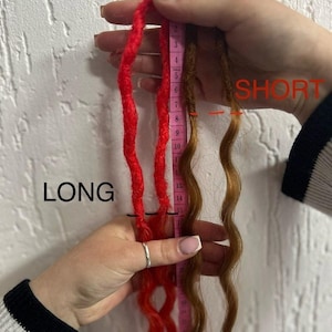 May include: Two sets of synthetic dreadlocks, one red and one brown, are shown next to a measuring tape. The red dreadlocks are 15 inches long and the brown dreadlocks are 8 inches long. The text "LONG" is written next to the red dreadlocks and the text "SHORT" is written next to the brown dreadlocks.
