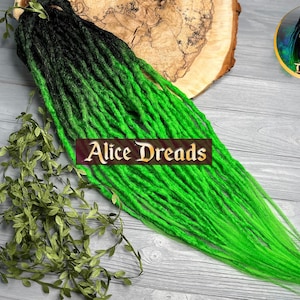 Könnte beinhalten: Schwarze und neongrüne Ombre-Synthetik-Dreadlocks. Die Dreadlocks sind lang und fließend, mit einer dunklen schwarzen Farbe an der Spitze, die allmählich zu einem leuchtenden Neongrün an der Basis übergeht. Die Dreadlocks werden auf einer Holzoberfläche mit grünen Blättern gezeigt.