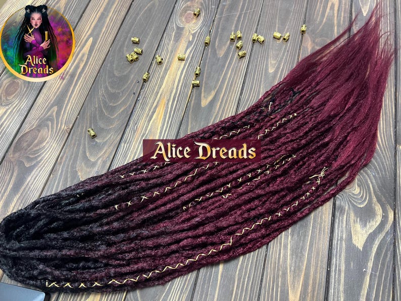 Synthetic dreads with black to burgundy ombre, available in 50-60 cm or 75-80 cm lengths. Features loose or dreaded ends with black and gold wrapped accents. Double Ended (DE) or Single Ended (SE) options.