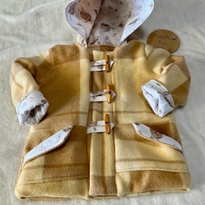 May include: A tan and cream plaid hooded coat with wooden toggle closures. The hood and cuffs are lined with a white fabric featuring a sea turtle and coral pattern. The coat has two front pockets.