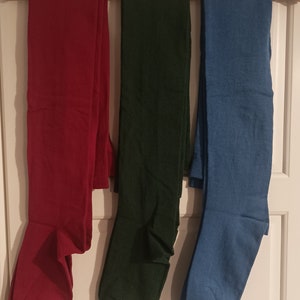 Op de afbeelding: Drie paar panty's hangen aan een houten hanger. De panty's zijn rood, groen en blauw.