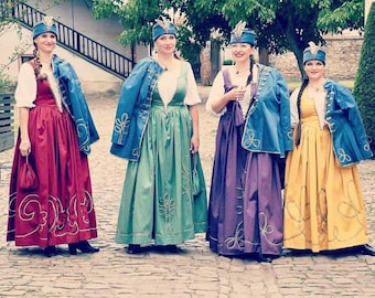 May include: Four people wearing traditional folk costumes. Each person is wearing a long skirt in shades of red, green, purple, and yellow. They also wear white blouses, blue jackets, and matching hats with feathers. The skirts have gold embroidery.
